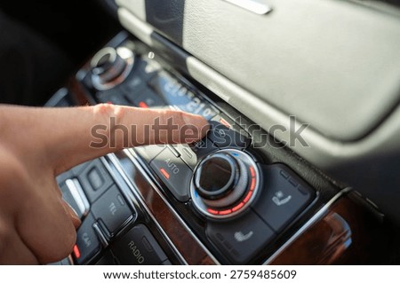 Finger presses air recirculation button on car climate control panel, adjusting airflow mode in vehicle interior with dual zone temperature display.