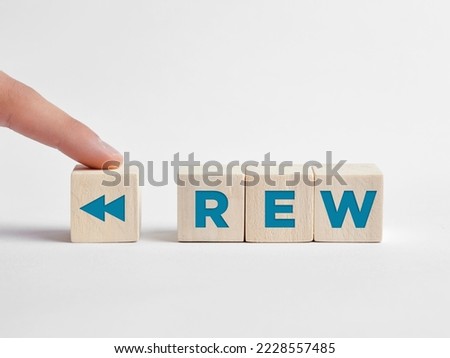 Finger presses the rewind REW button on wooden cubes.