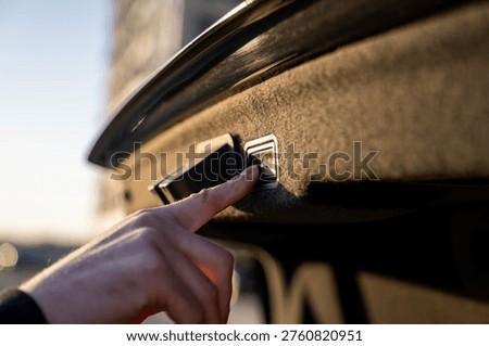 Finger pressing button for automatic trunk closing inside car, closeup of control panel on luggage compartment lid.