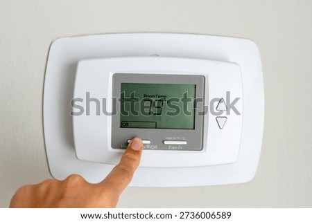 A finger pressing the button of a white temperature regulator, attempting to turn it on. The digital display is off, signaling a need for adjustment in the apartment's heating system
