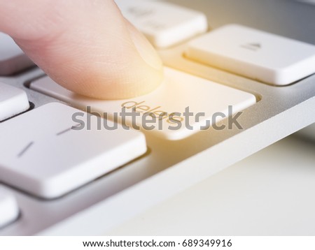 Finger is pressing delete key of a aluminum white computer keyboard