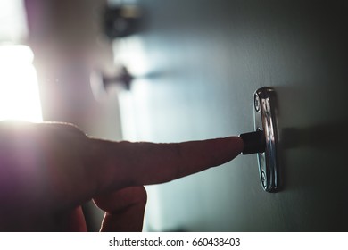 Finger Pressing Doorbell In Apartment Building Corridor. Close Up Of Male Hand Ringing Door Bell In A Block Of Flats. Unwanted Guest, Bad News Or Neighbor Complaining. Dramatic And Negative Feeling.