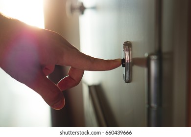 Finger Pressing Doorbell In Sunny Apartment Building Corridor. Close Up Of Male Hand Ringing Door Bell In A Block Of Flats. Salesman, Fundraiser, Guest Or Visitor Behind Door.