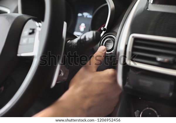 Finger pressing engine start\
button on car. The driver pushing on automatic start stop\
button.