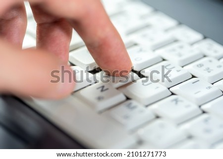 Finger pressing one single key on a white laptop keyboard, shallow dof, object macro, detail, extreme closeup. Using a computer, user experience, interaction, data input simple abstract concept