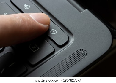 Finger pressing the power button on a black laptop computer.