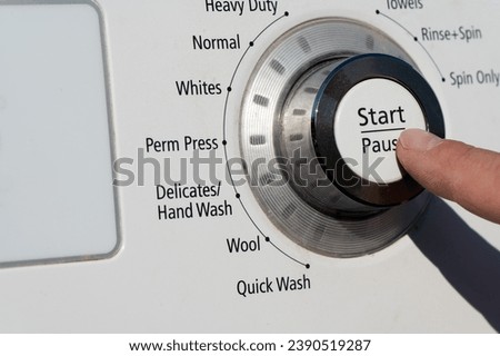 A finger pressing the start paude button on a washing machine