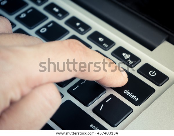 Finger pushing\
delete key on laptop\
keyboard