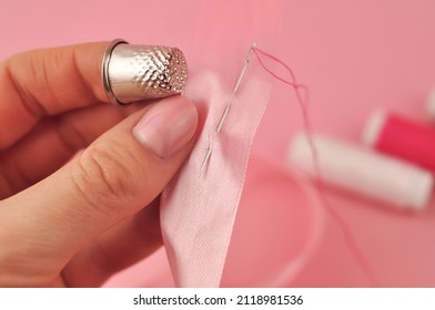 Finger with thimble hold sewing on pink background . High quality photo
