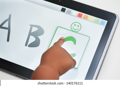 The finger of a toddler selecting the correct letter on a touchscreen tablet with learning software.