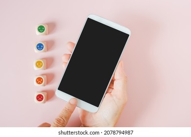 Finger Touch Mobile Phone With Clipping Path On Touchscreen And Blurred Emoticon Face On Wood Cube For Customer Review, Feedback, Rating, Ranking For Service Or Product, Mental Health Concept