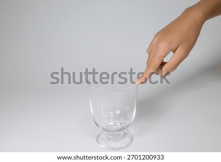 Finger touching the rim of an empty clear glass