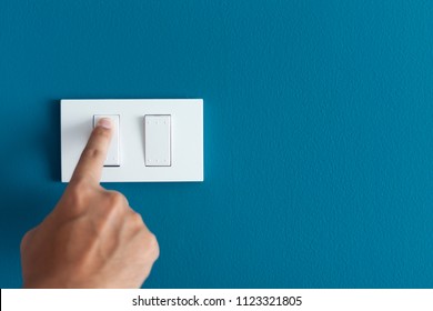 A finger turning on lighting switch on rough on blue dark wall. Empty space for text your