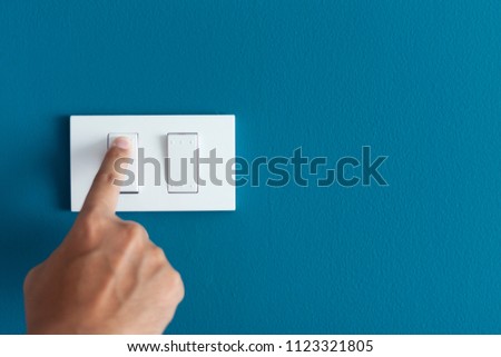 A finger turning on lighting switch on rough on blue dark wall. Empty space for text your