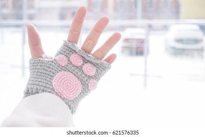 Fingerless gloves, a hand wearing handmade crochet fingerless gloves with pink cat paw in the middle, abstract blur background of snowing scenery on the back.