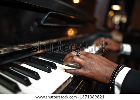 Fingers of african american man in black suit play piano.