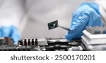 Fingers in blue gloves are holding a microchip with tweezers, close-up, blurry. Professional repair of electronic equipment