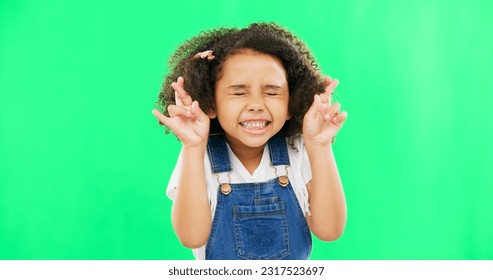 Fingers crossed, wish and praying with girl in studio for good luck, hope and optimism. Excited, emoji and closed eyes with child isolated on green background for miracle, positive and youth