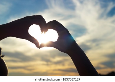fingers folded in a heart on a sunset background	