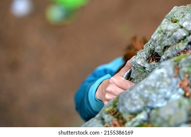 Fingers holding grey white limestone rock during sport climbing ascent with blurred brown leaves in the background