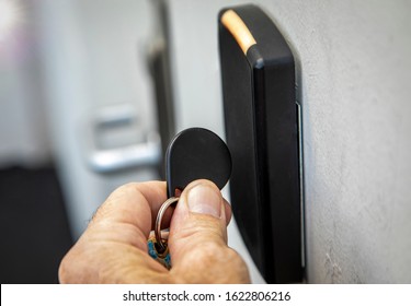 Fingers holding key fob on key fob sensor with door handle out of focus in the distance. 