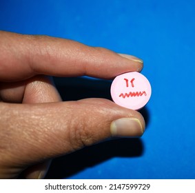 Fingers Holding Pill With Angry Face Drawing