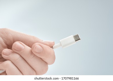 Fingers holding white type-c cable connector on a gray background.