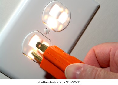 Fingers Inserting A Power Cord Plug Into A Glowing North American Standard 110 Volt Electric Wall Outlet Receptacle