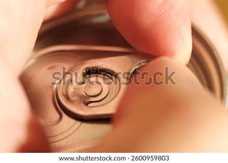 Fingers skillfully pulling the ring tab of an aluminum can, revealing a cold, refreshing drink that quenches thirst in moments of anticipation and enjoyment