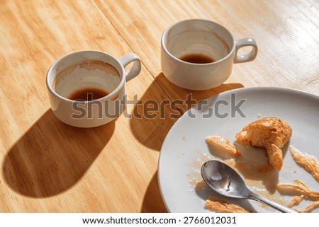 Finished breakfast. Empty espresso cups and croissant crumbs on white plate in morning sun rays from window. Finished morning coffee for couple. View of served table after coffee break.