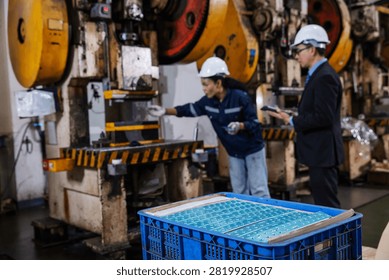 Finished precision metal components in the foreground while engineers inspect an industrial stamping machine in a modern manufacturing factory. 