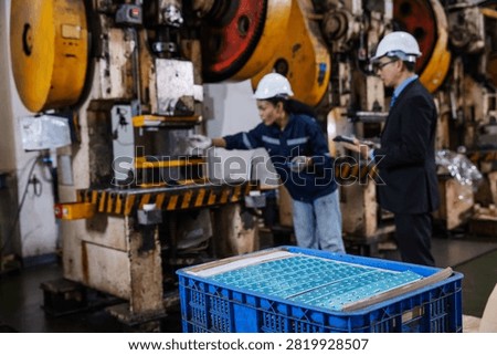 Finished precision metal components in the foreground while engineers inspect an industrial stamping machine in a modern manufacturing factory. 