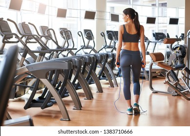 Finishing workout. Back view of short and slim young woman in sportswear standing at gym with jump rope