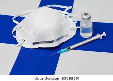 Finland Flag, N95 Face Mask, Needle Syringe And Vial. Concept Of Covid-19 Coronavirus Vaccine Distribution, Supply Shortage And Healthcare Crisis