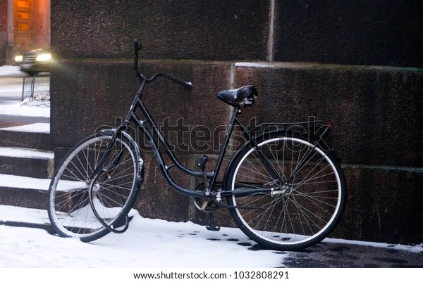 Finland, Helsinki, January 2018:\
a Bicycle stands at the wall and a car with headlights is passing\
by