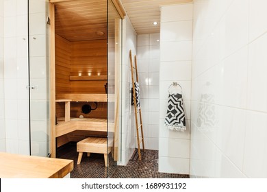 Finnish bathroom with a small wooden sauna and mosaic tile floor. Modern spa interior with glass door and Turkish towel.