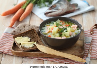 Finnish creamy salmon soup Lohikeitto on a wooden tray served with rye bread, butter, and greens