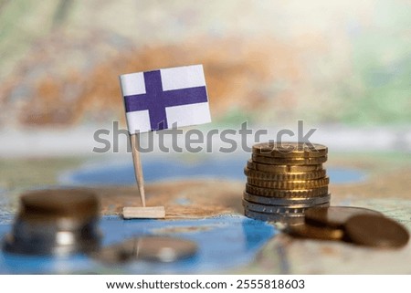 finnish flag and coin stack on a map, symbolizing economy, trade, finance, investment, savings, national policy, economic growth, blurred background