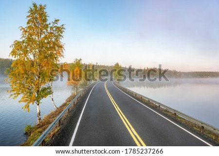 Finnish landscape with narrow car road through the lake. Foggy early morning in autumn in Finland