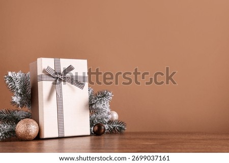 Fir tree branches, gift box and other Christmas decor on wooden table against brown background. Space for text