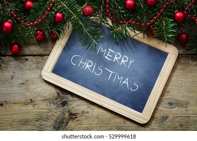 Fir tree branches with red christmas balls and a writing  board on rustic wooden planks, sample text Merry Christmas - Shutterstock ID 529999618
