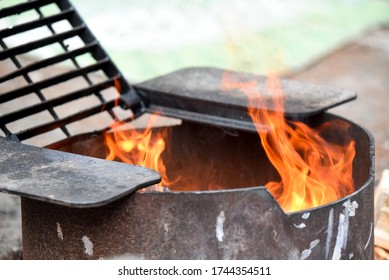 Fire In Black Metal Pit With Grate At Campsite