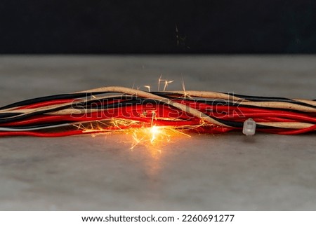 fire burns in twisted electric wires, sparks fly on a dark background. A short circuit in the electrical wiring, the cause of the fire. Flames and smoke.