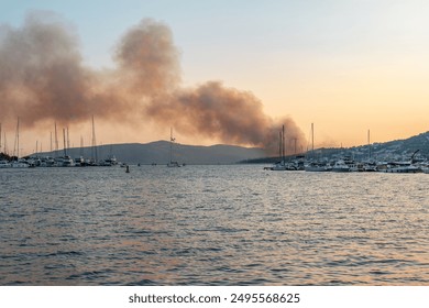 Fire in Croatia, near Split and Trogir, produces a large plume of smoke visible against a dramatic sunset. Yachts are seen on the sea, with mountains forming a striking horizon backdrop. - Powered by Shutterstock