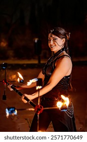 Fire dancer smiling while showcasing skillful movements with a flaming staff during an energetic nighttime performance under the stars