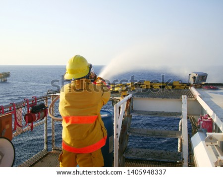 Fire drill or emergency drill training on board for the crew in ship at offshore living quarters, helideck offshore plant form of oil and gas industrial with fireman, fire hose, water spray to the sea