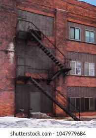 Fire Escape Stairs And A Bicycle Outside A Brick Apartment Building In Winter