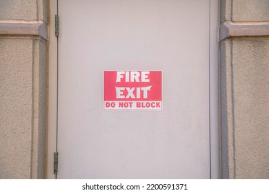 Fire Exit Do Not Block On A Beige Door At Downtown Tucson, Arizona. Close Up Of A Fire Exit Sign On A Door With Side Hinges In Between The Concrete Walls.