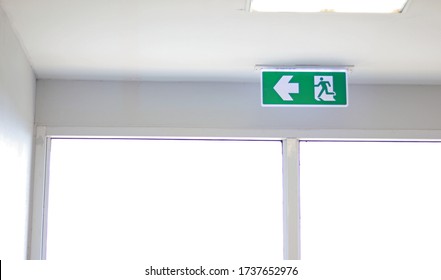 Fire Exit Sign On The Ceiling Entry The Fire Escape, Green Safety Light Symbol Isolated In White Window. Caution For Warning In Dangerous Fire Situation, Risk Assessment Management Safety Workplace.