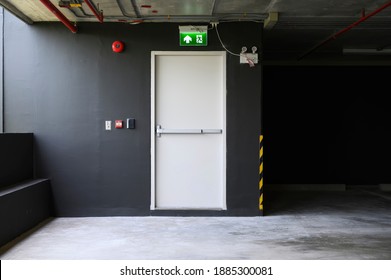 A fire exit with the sign and red alarm bell above the white door on the parking building.